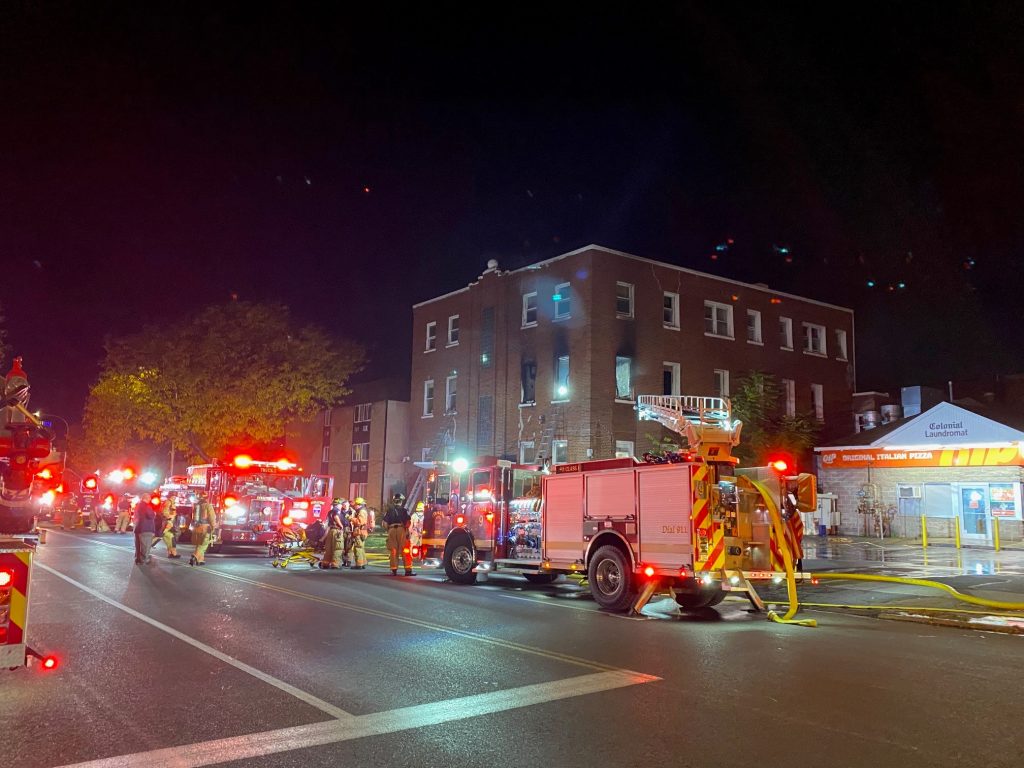 A second view of the northeast corner of the building, with various fire apparatus placed at the scene, as well as ladders placed to windows on the second floor.